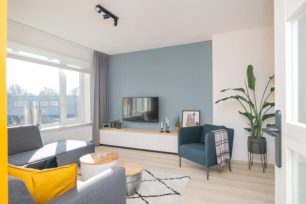 Scandinavische stijl woonkamer met licht eiken vloer, hoekbank, fauteuil, tv meubel. Renovatie appartement in Voorburg.